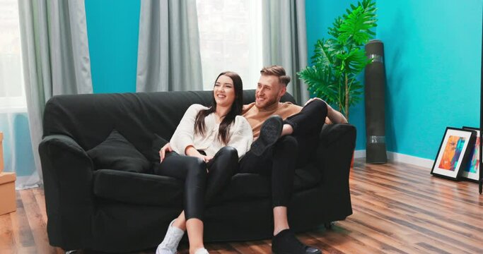 Happy European couple planning renovation and furnishings in new house, sitting on comfortable sofa, excited man sharing ideas with attractive woman in living room.