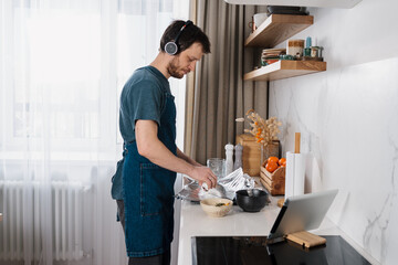 Adult man making dorado fish by video recipe and listening to social media audio chat on headphones