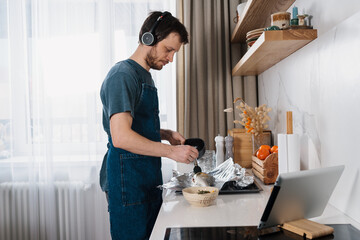 Adult man making dorado fish by video recipe and listening to social media audio chat on headphones