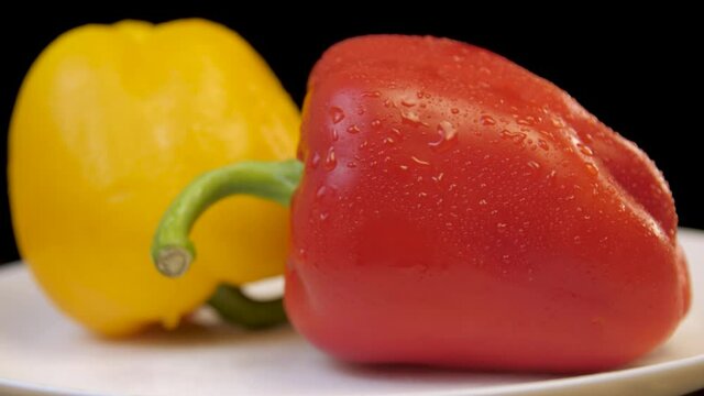 Raw red and yellow bell peppers rotate on a whait plate