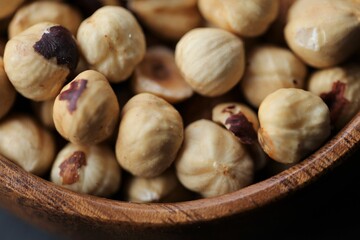 Hazelnuts peeled in a wooden round cup on a black shabby board background.Healthy food and snack.
