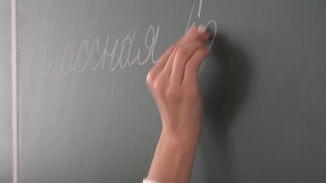 School teacher writes with chalk on the blackboard classwork
