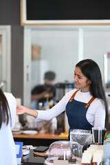 Portrait of beautiful barista recommending and accepting orders from customers in modern coffee shop.