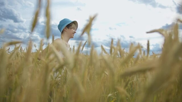 funny boy in a blue hat running across a golden wheat field and smiling