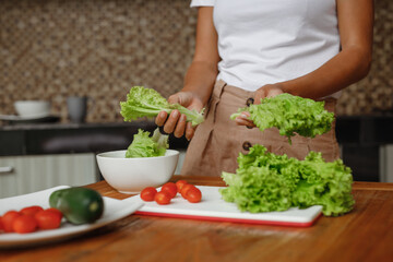 Cropped image unrecognisable woman cooking healthy food at home kitchen - lettuce salad, cherry toatoes and cucumber