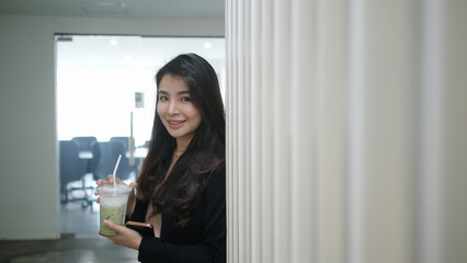 Smiling businesswoman holding plastic cup of fresh juice while standing in office.