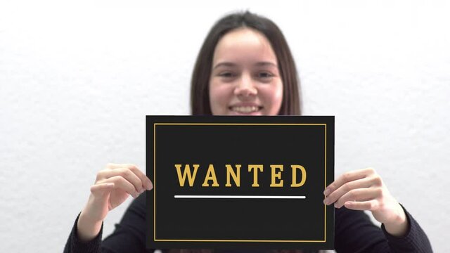 Conceptual message "Wanted" on canvas frame label hold by beautiful girl smiling at camera