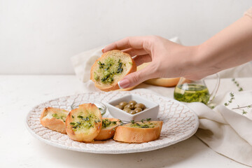 Female hand and fresh bread with garlic sauce on light background
