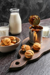 Tasty cookies and tin can of boiled condensed milk on dark background