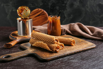 Tasty wafer rolls with boiled condensed milk on dark background
