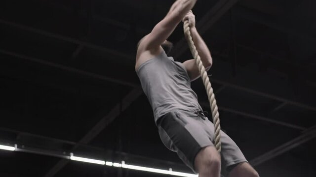 Low angle view of middle-aged Caucasian man wearing sportswear climbing a tightrope in gym