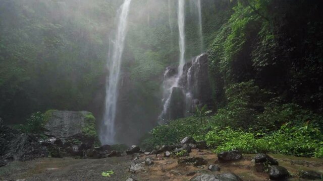 Slow motion tilt up of rushing waterfalls in a misty rainforest with glistening rocks and lush tropical plants - Bali, Indonesia