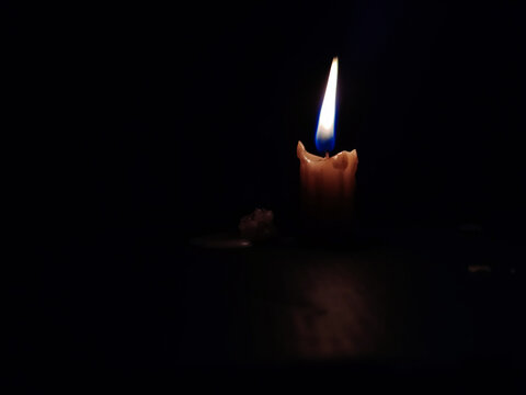 Stock photo of a burning little white color candle with calm yellow and blue color flame with dark black background. focus on object.