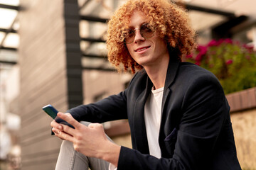 Young redhead man using smartphone on street