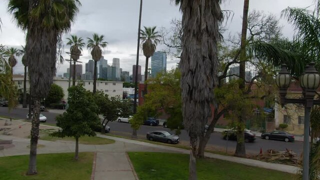Aerial rising shot of downtown from a distant neighborhood park under cloudy gray skies - Los Angeles, California