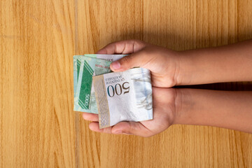 niño de primera vista con las manos abiertas sosteniendo 500 bolívares sobre la mesa, dinero venezuela, concepto de finanzas