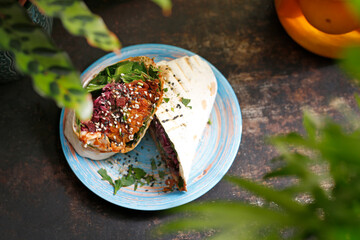
Falafel in pita bread. Vegetarian street food. Tasty colorful healthy dish served on a background of green plants. Suggestion to serve the dish. Culinary photography.