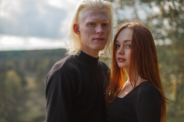 Fototapeta premium A young couple guy and a girl stand in nature against a backdrop of green trees and look straight into the camera. Walking in nature. High quality photo