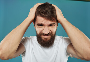 Upset man with a beard touches his head with his hands on a blue background