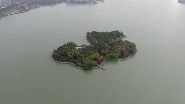 Aerial panning shot of green trees on island at Jinji Lake near city, drone flying during sunny day - Suzhou, China