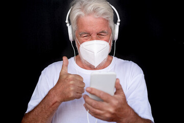 Close-up of attractive senior man using phone wearing surgical mask. Elderly retiree enjoying social and tech. Black background