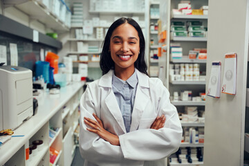 Cheerful young african american female pharmacist wearing labcoat with folded hands standing in chemist near shelves - 418259641