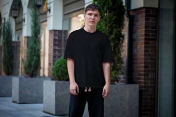 Fototapeta na wymiar Mockup of a black T-shirt on a guy in dark pants, stylish clothes in an urban style on a blurred street background.