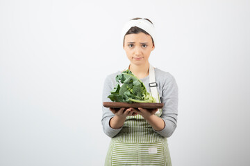 Picture of a young attractive woman holding a wooden plate of broccoli