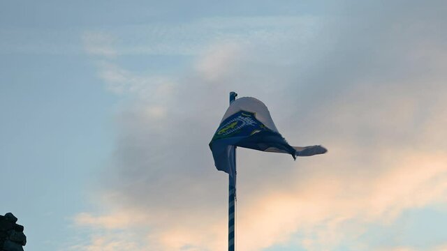 Flag of small town Kamnik waving in light breeze on top of ruins of old castle. Beautiful lights of sunset in Slovenia. Static shot, real time, close up view