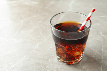 Glass of cola with ice cubes and straw on gray table