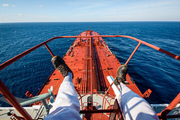 Legs of a worker sitting on top of the radar mast of crude oil super tanker