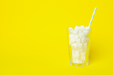 Glass with sugar cubes and straw on yellow background