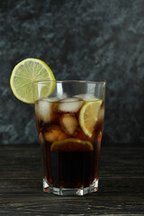 Glass of Cuba Libre on wooden table against black smokey background