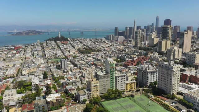 Aerial shot of city by famous bridge over sea against sky, drone flying forward over modern cityscape on sunny day - San Francisco, California