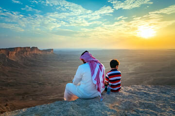 An arab man and his son sitting on Edge of the world, a natural landmark and popular tourist...