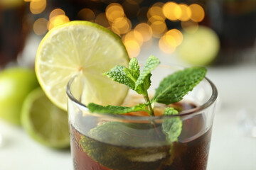 Glass of Cuba Libre against blurred lights, close up