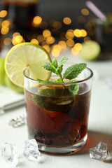 Glass of Cuba Libre on white textured table against blurred lights