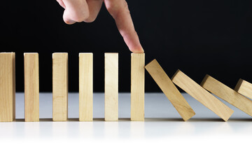 Closeup image of a finger try to stop falling wooden dominoes blocks for business crisis effect or...