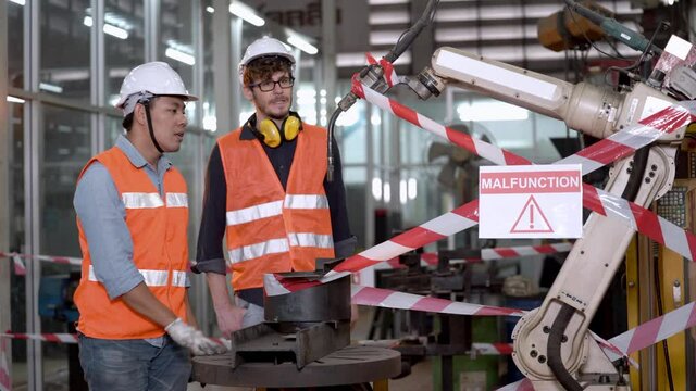 factory worker engineers talking about machine out of order and broken. young inspector people men checking technology equipment in factory. robot is malfunction with red white line danger signage.