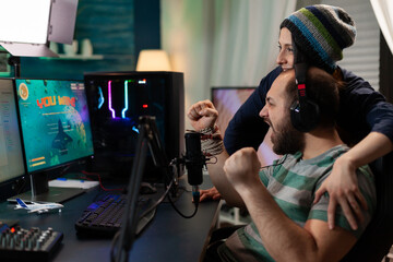 Streamer couple winning online space shooter competition using professional headset, microphone, keypad. Gamer playing online videogames with new graphics on powerful computer