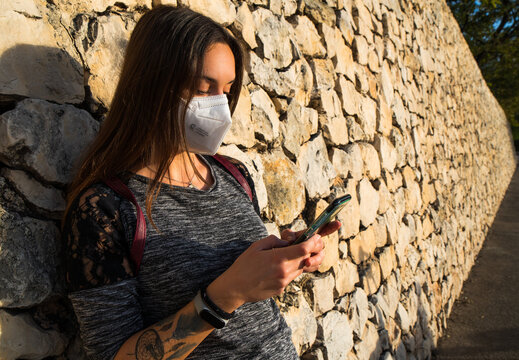 Girl with a mask sends a message on her cell phone.