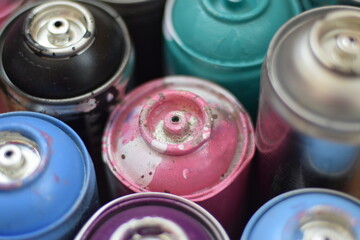 Large number of used colorful spray cans of aerosol paint lying on the treated wooden surface in...