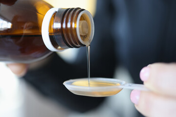 Woman pouring medicinal syrup into measuring spoon closeup