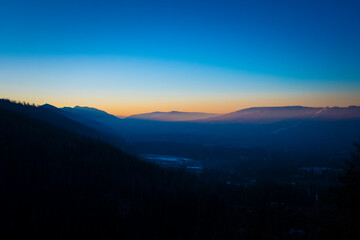 Obraz premium Clear blue sky over Podhale region, Poland. Orange sunset illuminates the ridge of Tatra Mountains. Selective focus on the silhouette of the hills, blurred background.