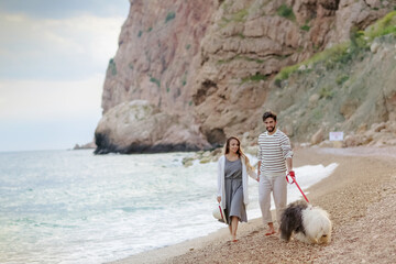 Happy young couple walking with big dog on the beach in summer.