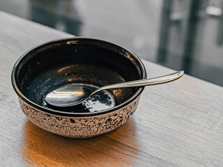 Metal spoon inside empty dirty plate after meal with  stands on wooden table near window. Black and white soup plate
