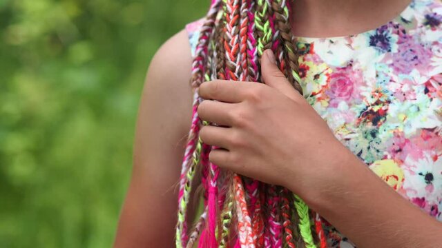 A teenage girl strokes her colorful dreadlocks with her hand.