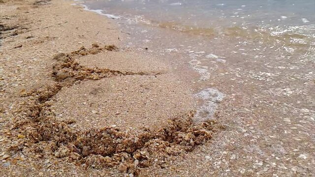 A woman draws a heart on the seashore which is washed away by a wave. The wave washes away the heart nestled in the sand. Woman draws a heart in the sand