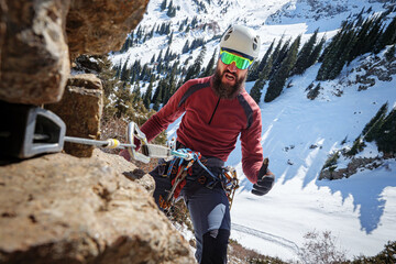 Frightened bearded climber hangs on the belay. High-altitude mountaineering in winter. A man climbs...