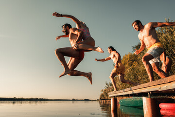 Young friends having fun enjoying a summer day swimming and jumping at the lake.
